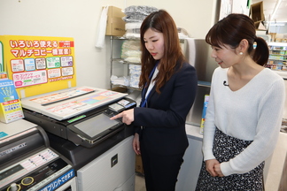 コンビニでの端末利用について職員がレポーターに説明する様子